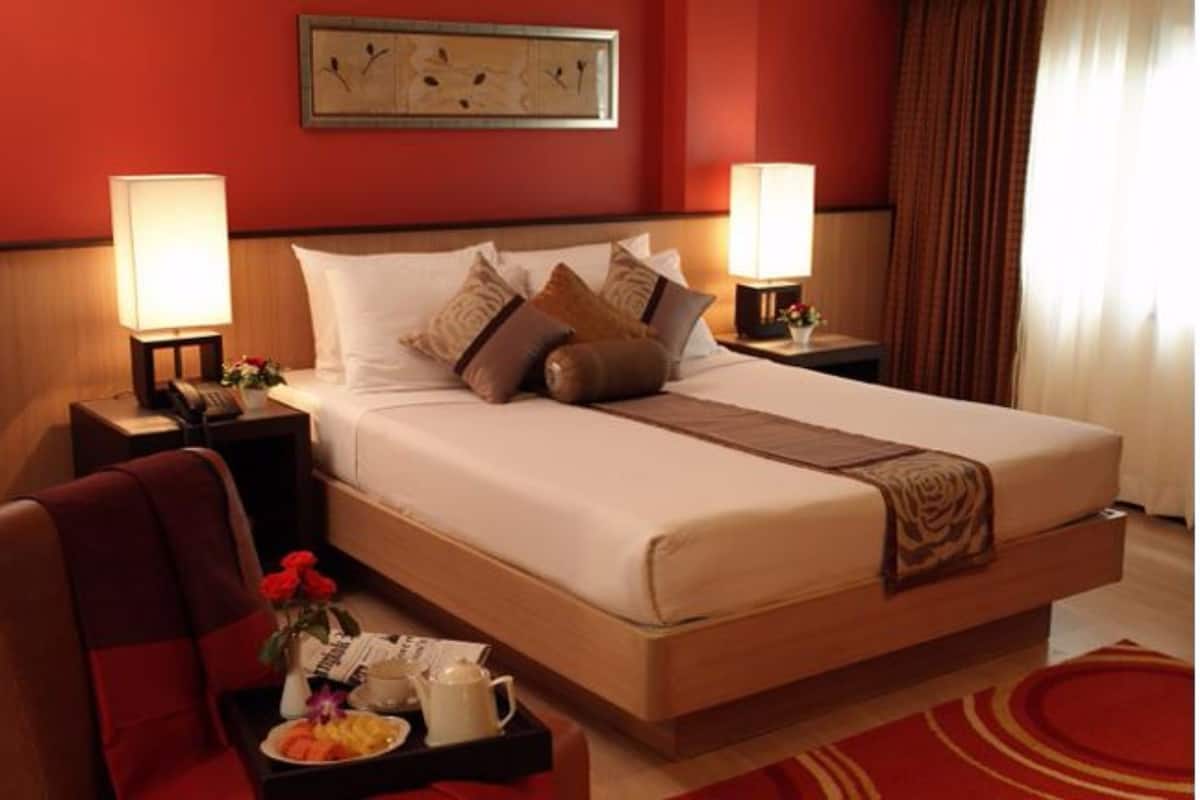A hotel room with a large bed, two bedside lamps, a nightstand with a lamp, a chair, a tray with breakfast items, and a painting on the wall.