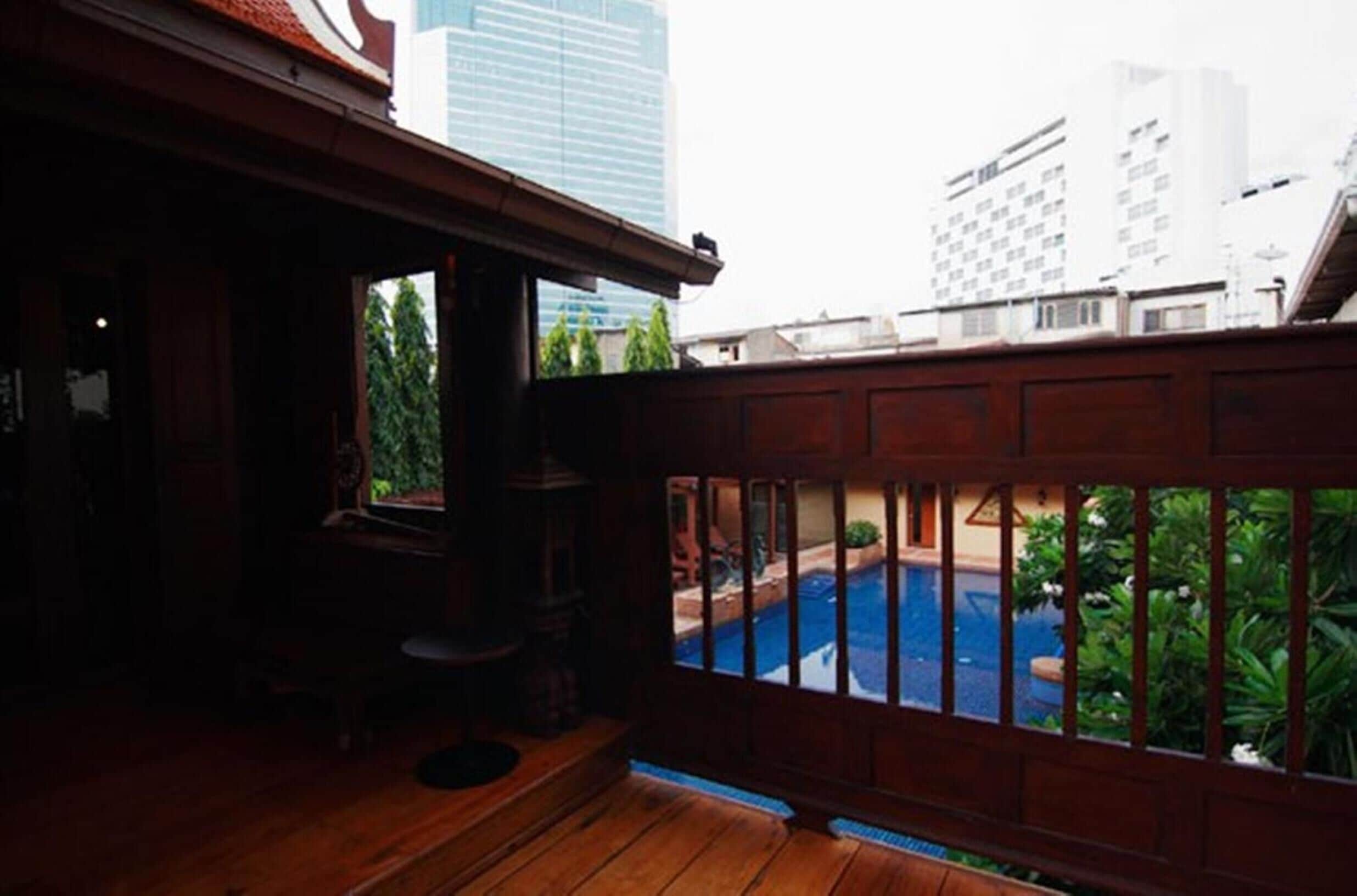 A wooden balcony with a view of a swimming pool and surrounding greenery.