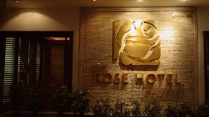 Entrada de hotel con un gran letrero iluminado que dice "Rose Hotel Bangkok".