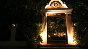 Una entrada bien iluminada con el nombre "Ruen Urai" en la parte superior, rodeada de plantas en macetas y un arco decorativo.