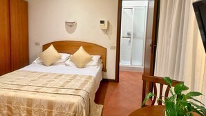 Un dormitorio con cama, un armario de madera, una mesita de noche con una planta y un baño con ducha.