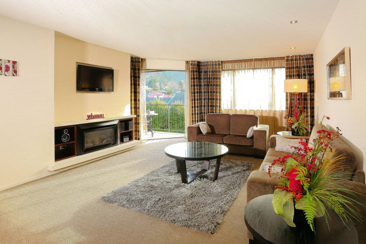 A living room with a sofa, a coffee table, a flat-screen TV mounted on the wall, and a fireplace.
