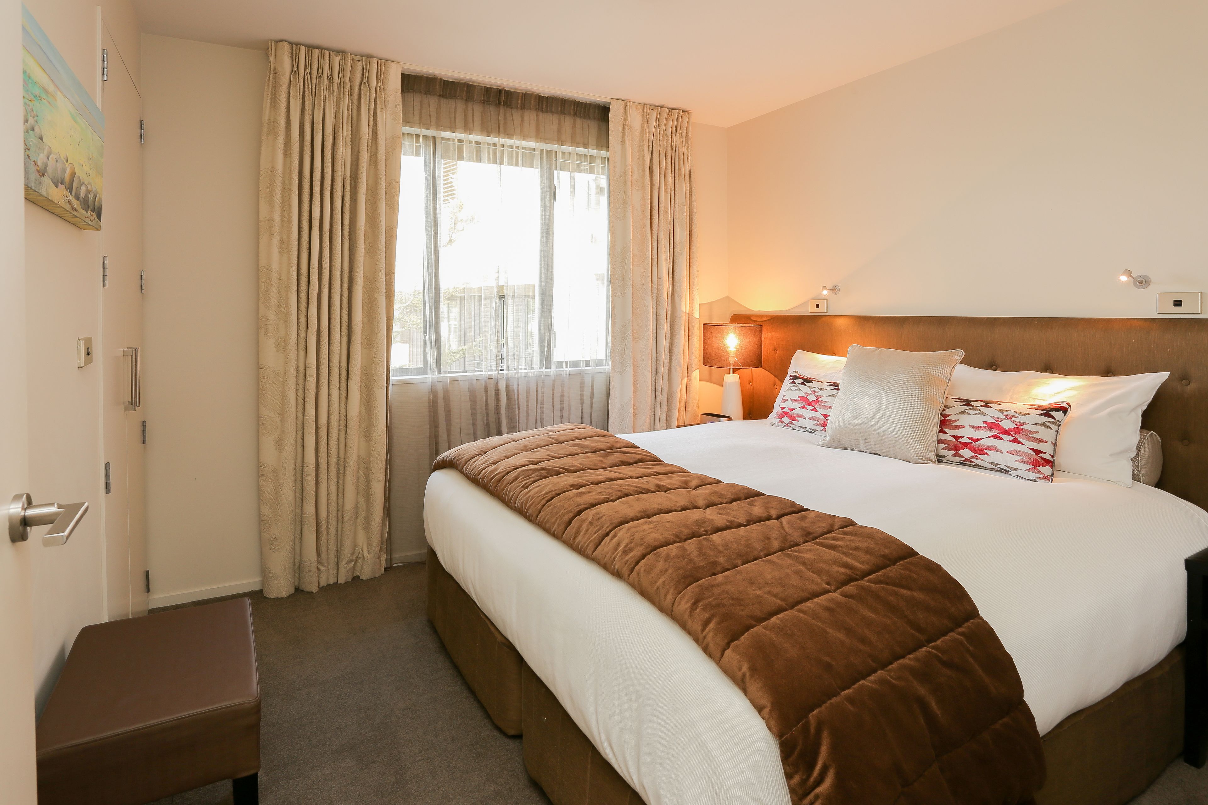 A hotel room with a large bed, a bedside lamp, and a window with curtains.
