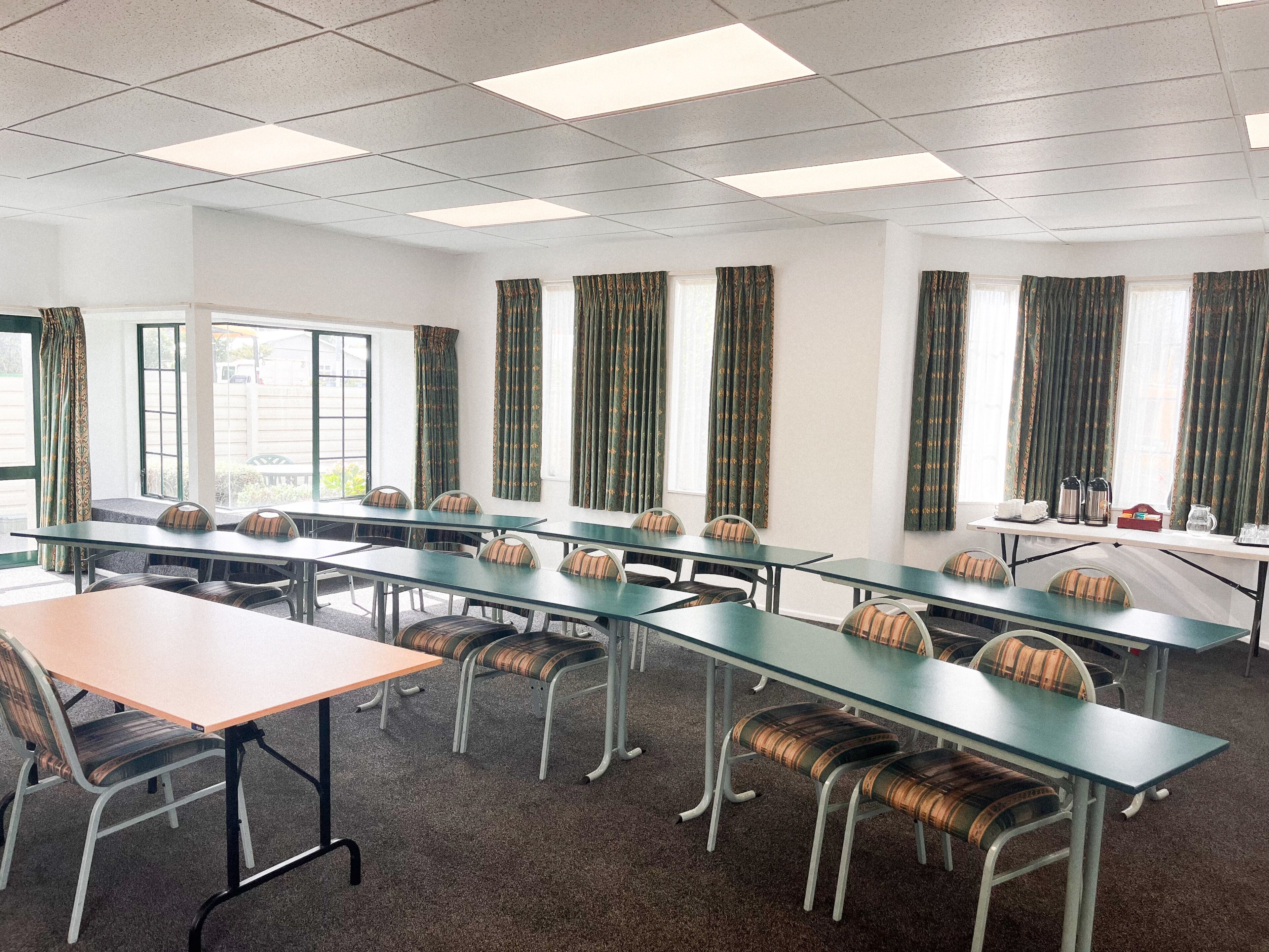 Una sala de conferències amb diverses taules i cadires, grans finestres amb cortines i un sostre amb llums fluorescents.