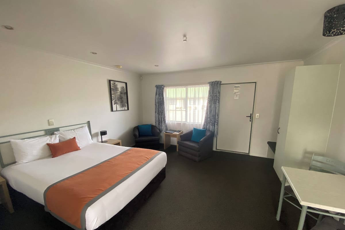 A hotel room with a bed, two chairs, a desk, and a wardrobe.