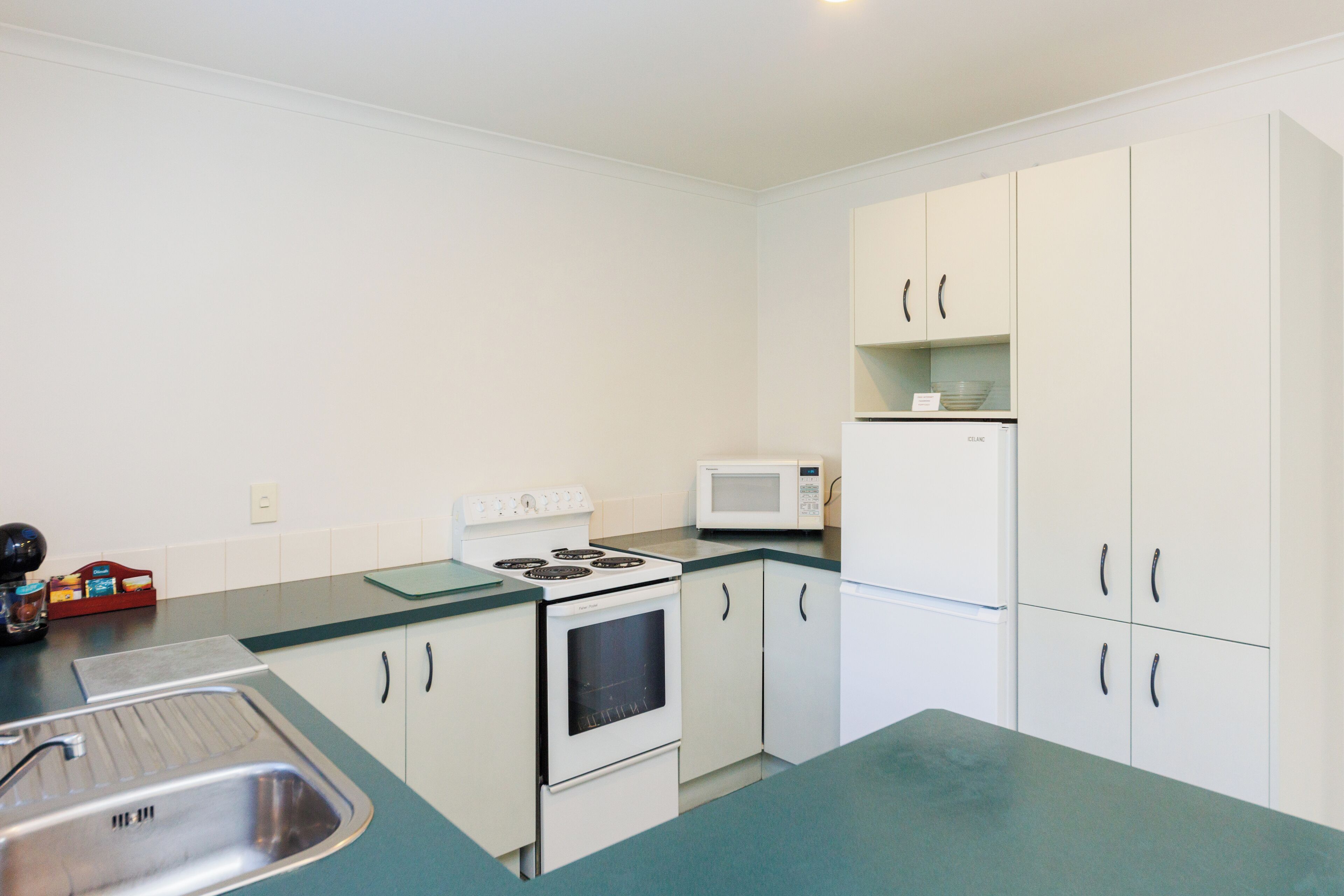 A compact kitchen with white cabinets, a stove, a microwave, and a sink.