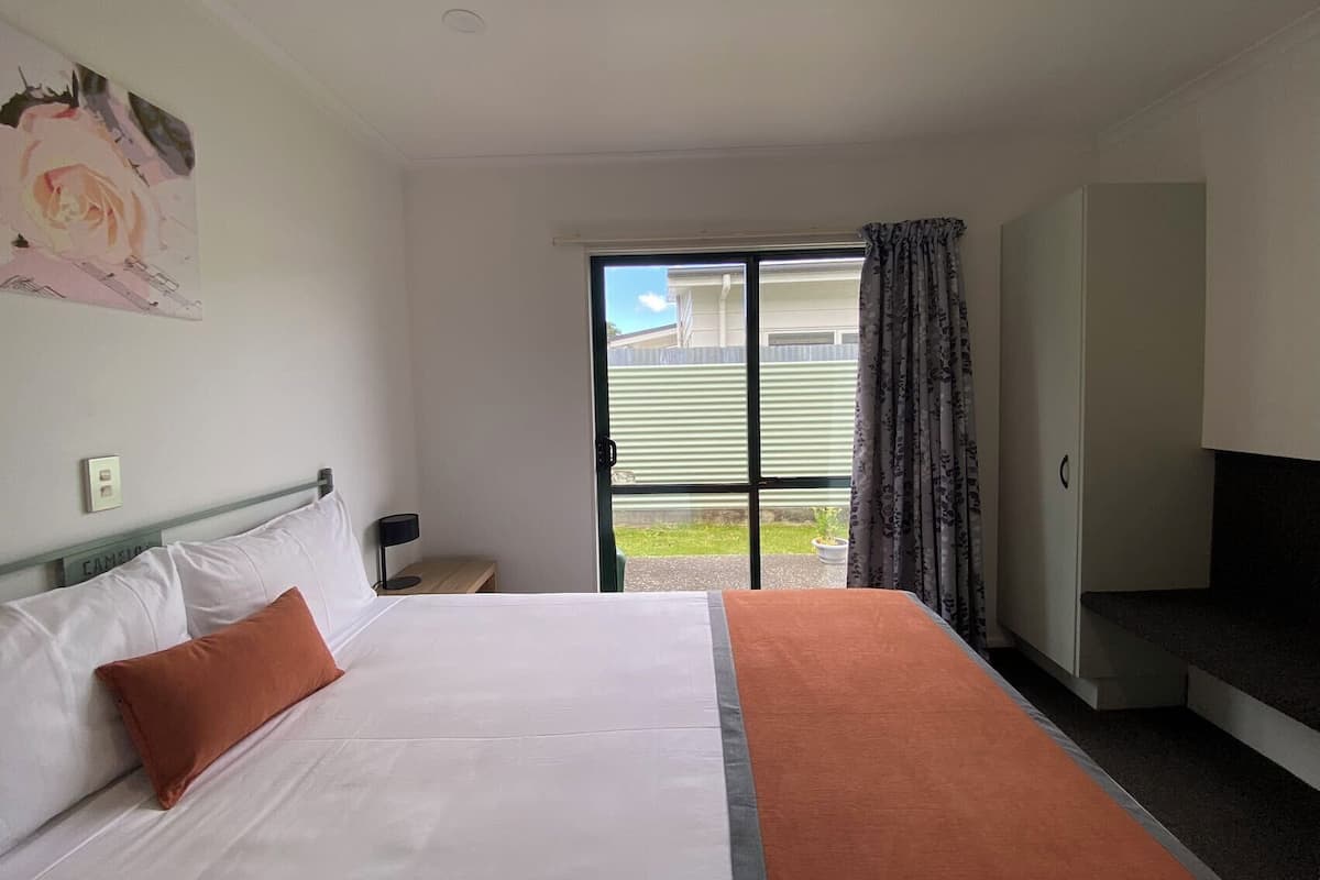 A hotel room with a bed, a television, and a sliding glass door to the outside.