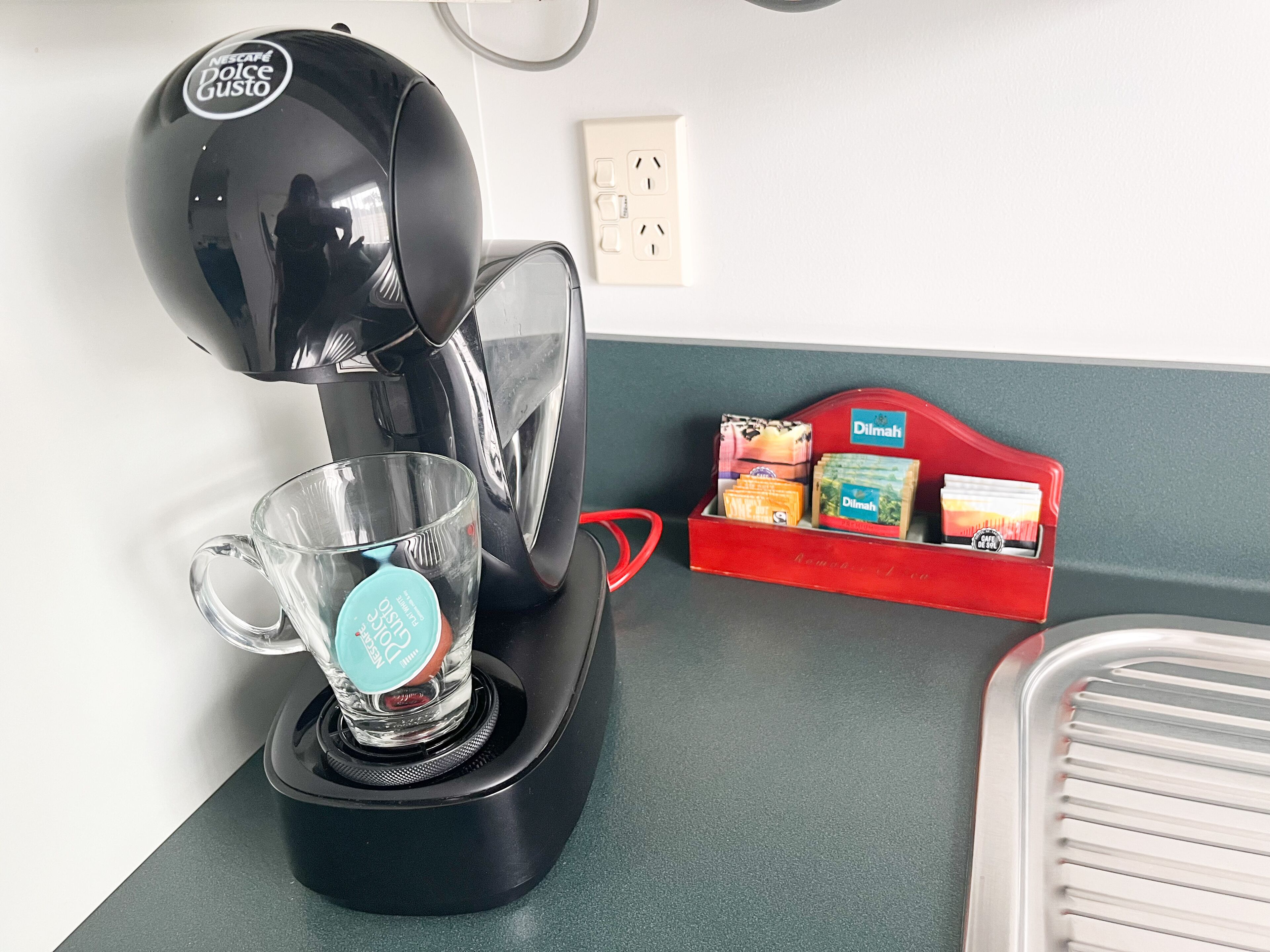 A coffee maker with a glass cup and a red box of snacks on a kitchen counter.