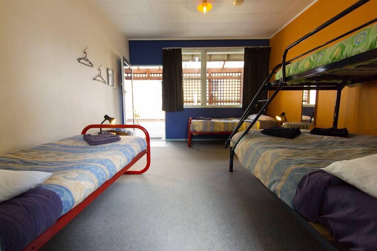 Une chambre de dortoir avec deux lits simples, un lit superposé, une fenêtre avec des rideaux et une porte.
