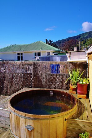 A wooden hot tub on a wooden deck with a view of a house and mountains in the background. - Sequoia Lodge & Backpackers (Picton)