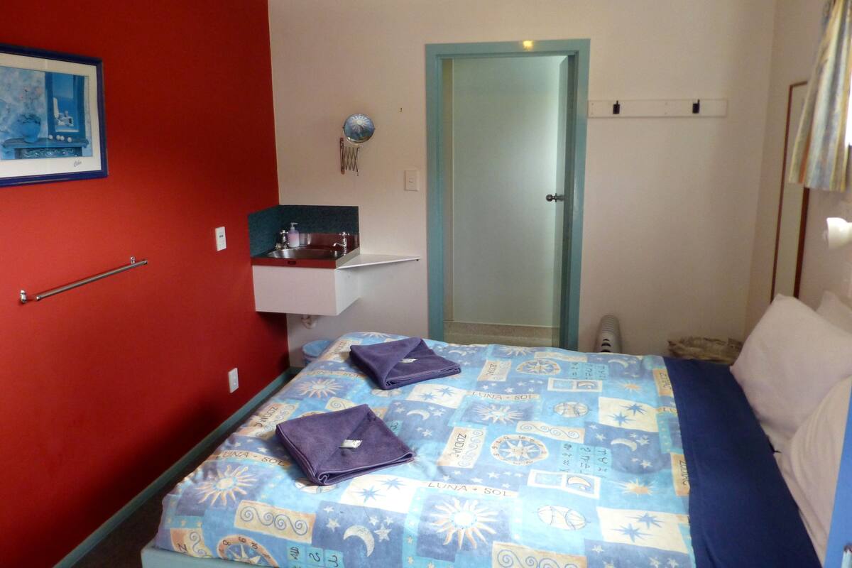 Une chambre à coucher avec un lit, une petite table de chevet, un miroir et un mur rouge.