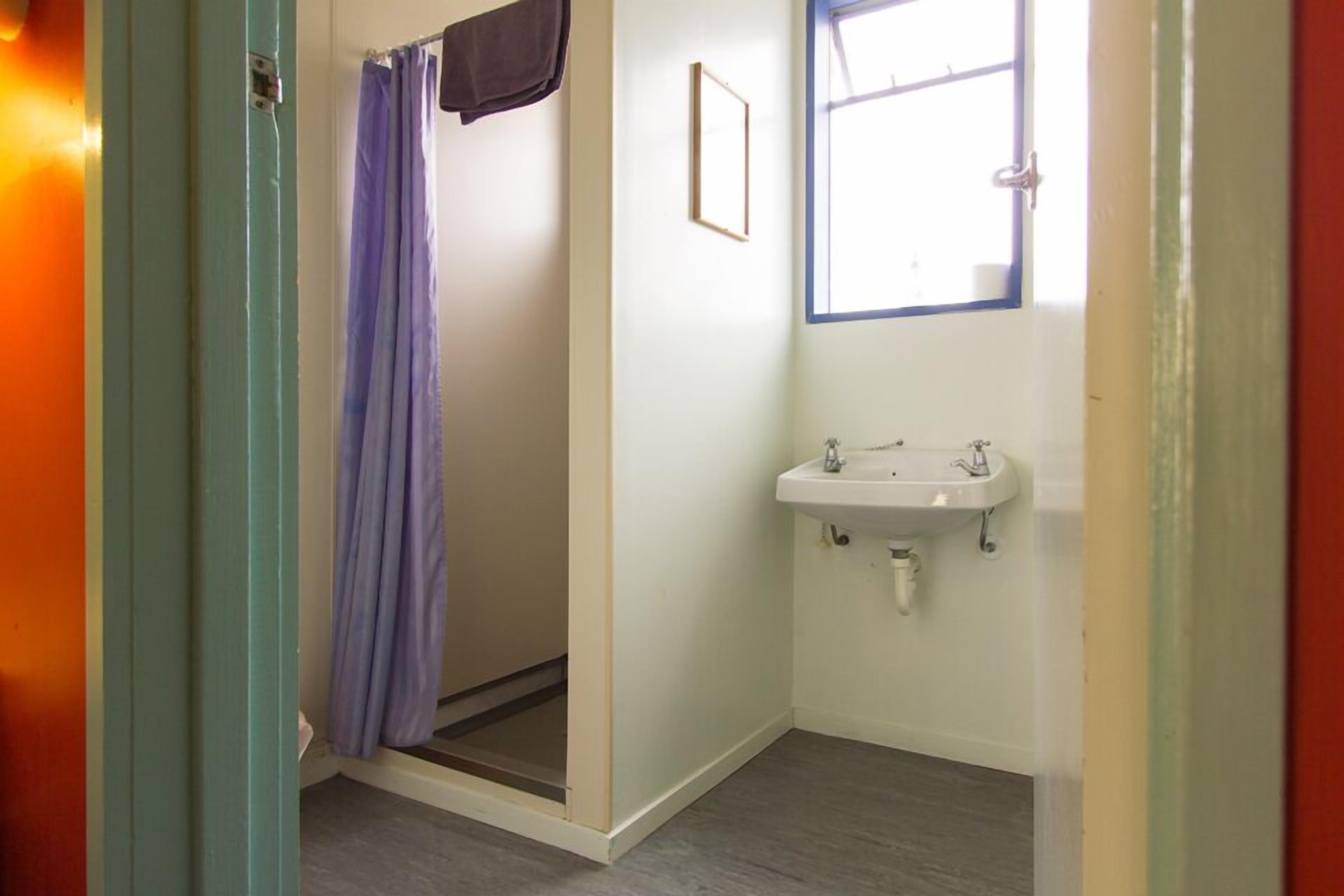 Een badkamer met een douche, een wastafel en een raam.