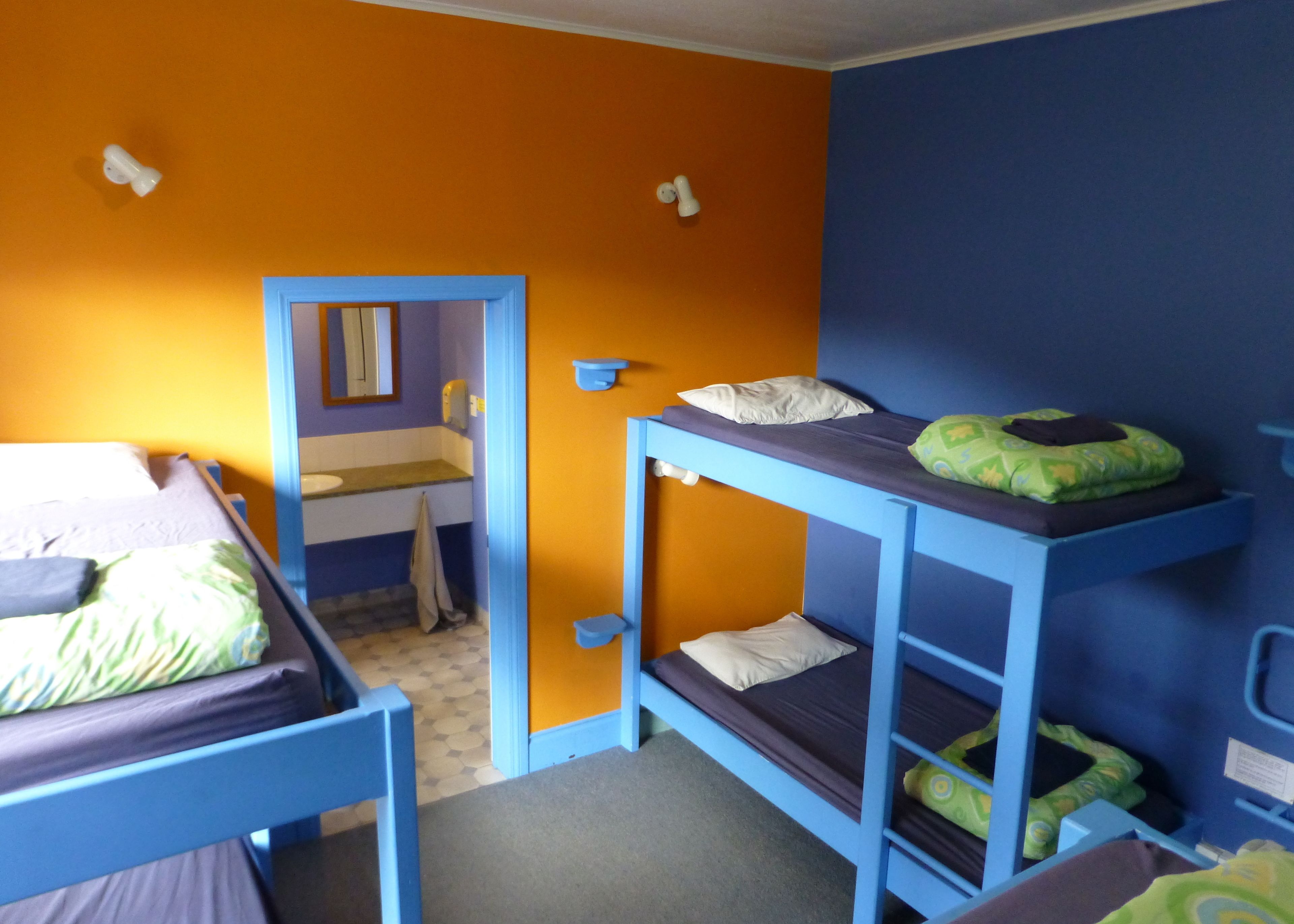 A dormitory room with bunk beds, a bathroom with a mirror, and a sink.