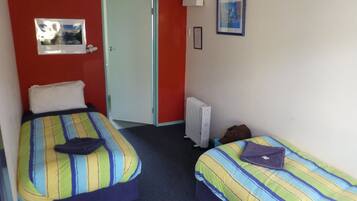 A room with two beds, each with striped bedding, a radiator, a door, and a framed picture on the wall.