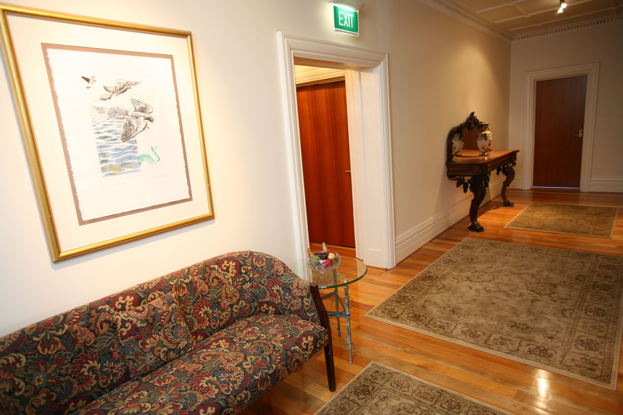 Ein Korridor mit einem gemusterten Sofa, einem gerahmten Kunstwerk, einem Glastisch mit einer Schale und einem Teppich.