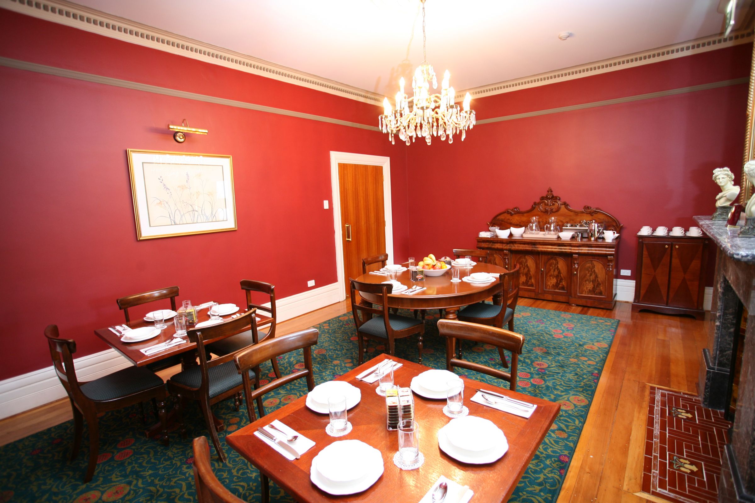A dining room with a red wall, a chandelier, and a wooden dining table set for four.