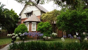 Una casa con fachada de ladrillo, techo a dos aguas y un jardín bien cuidado con diversas flores y arbustos.