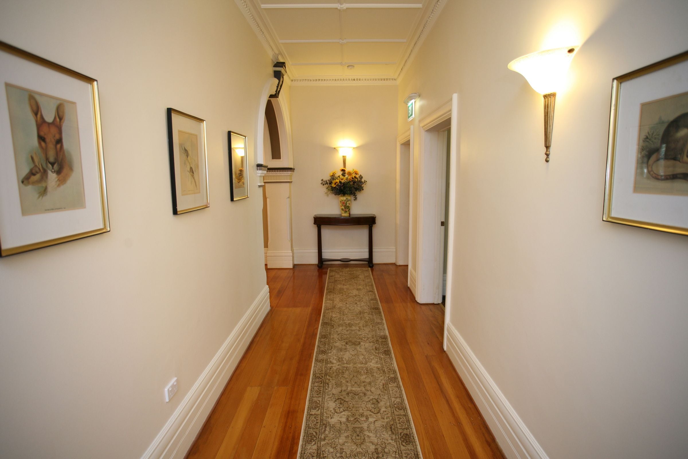 A hallway with framed artwork on the walls, a wooden floor, and a central rug.