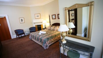 A hotel room with a bed, two chairs, a desk with a lamp, a mirror, and framed pictures on the wall.