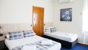 A hotel room with two beds, a wooden door, an air conditioning unit, and a painting on the wall.
