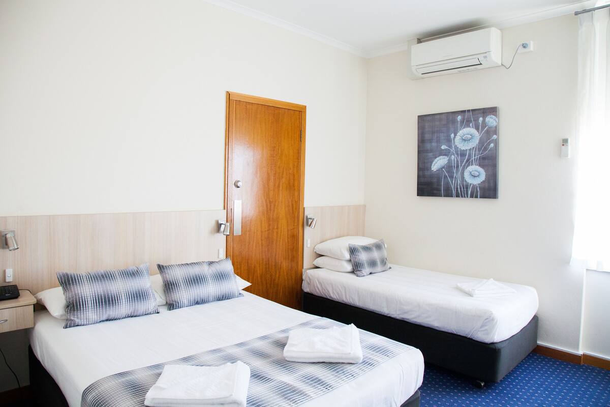 Quarto de hotel com duas camas, porta de madeira, unidade de ar condicionado e um quadro na parede.