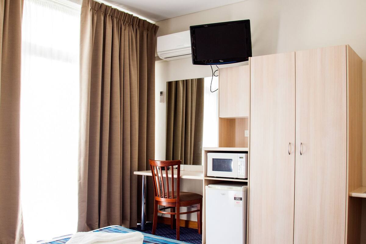 Quarto de hotel com cama, escrivaninha com micro-ondas, televisão e guarda-roupa.
