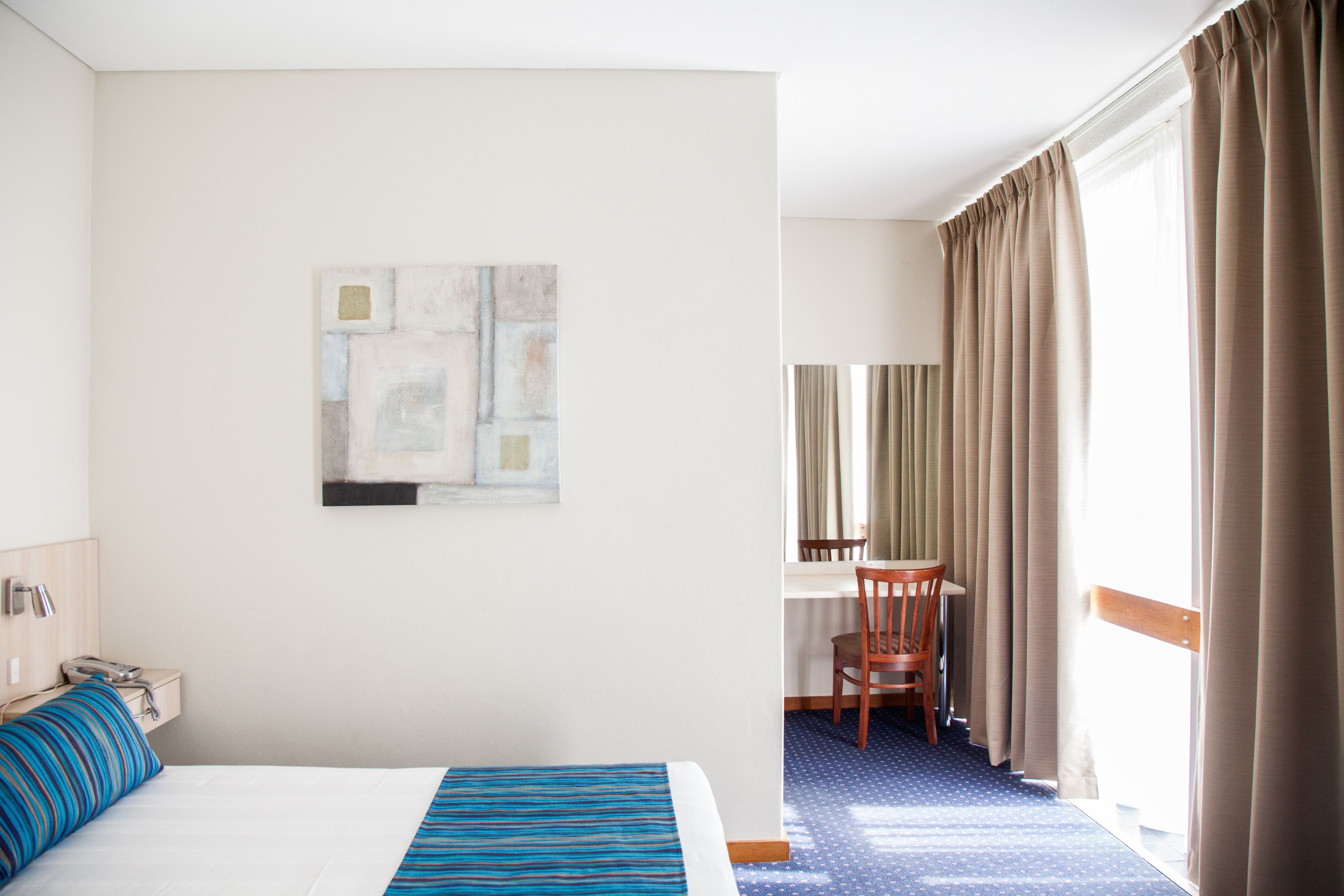 A hotel room with a bed, a desk, a chair, and a window with curtains.