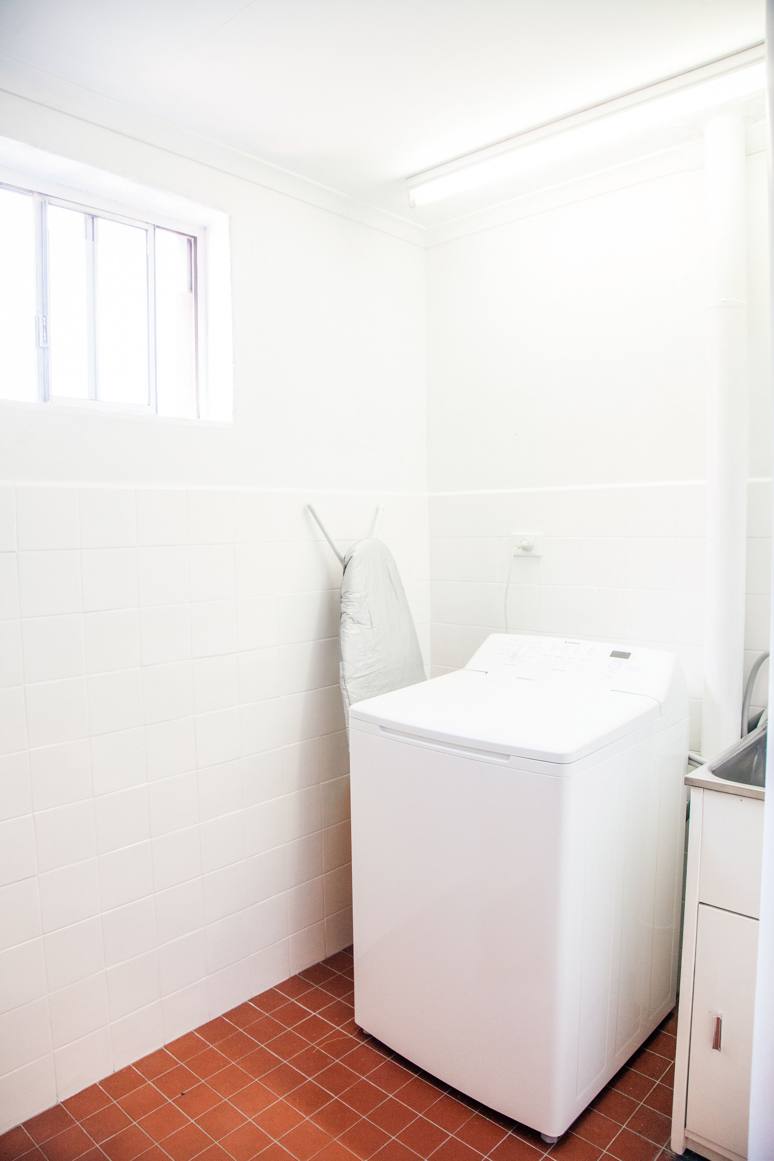 A compact, white laundry room with a washing machine and a drying rack.
