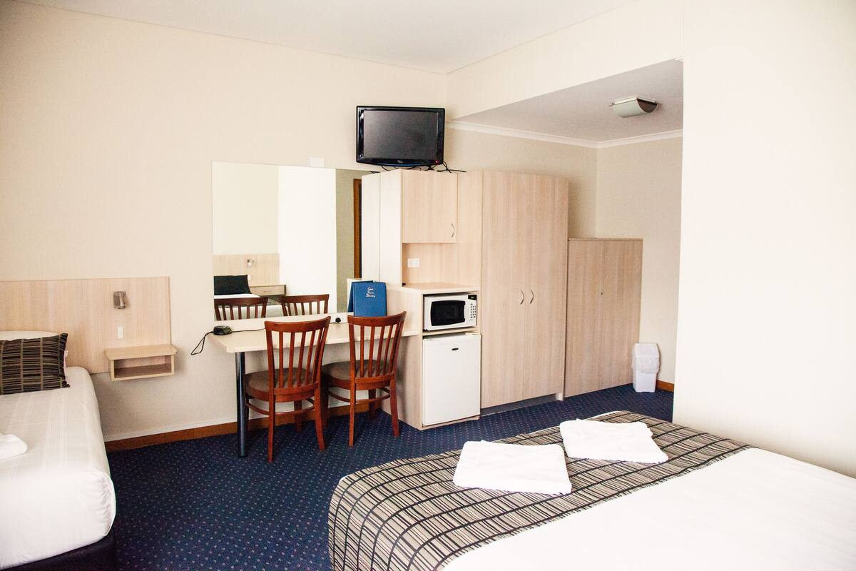 Quarto de hotel com cama, secretária com cadeira, micro-ondas e televisão.