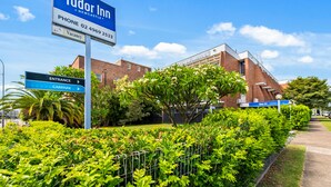 A Tudor Inn sign with directions to the entrance and car park, surrounded by well-maintained greenery and a clear sky.