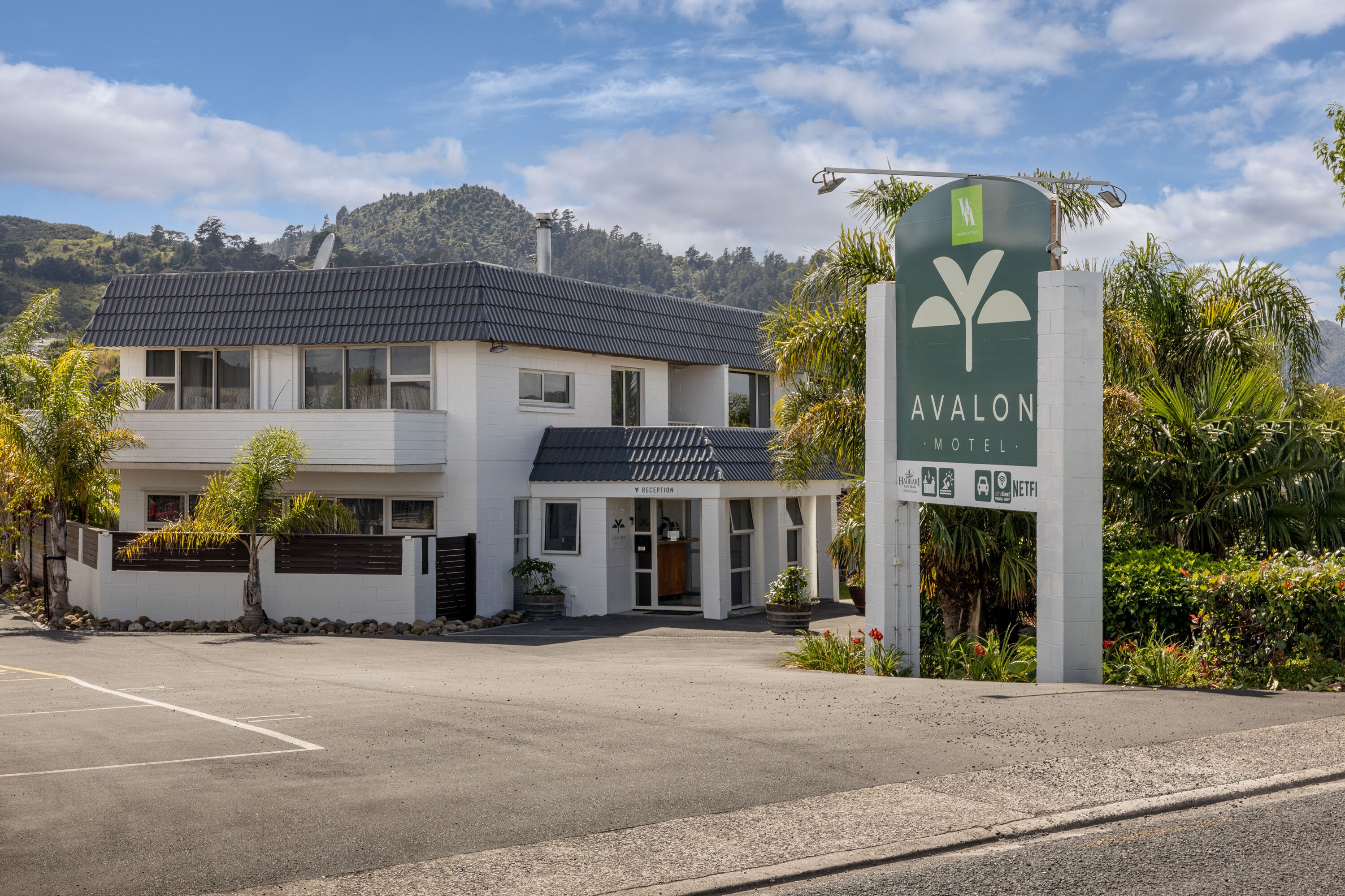 A two-story building with a reception area, labeled "Avalon Motel," surrounded by greenery and a mountainous backdrop.