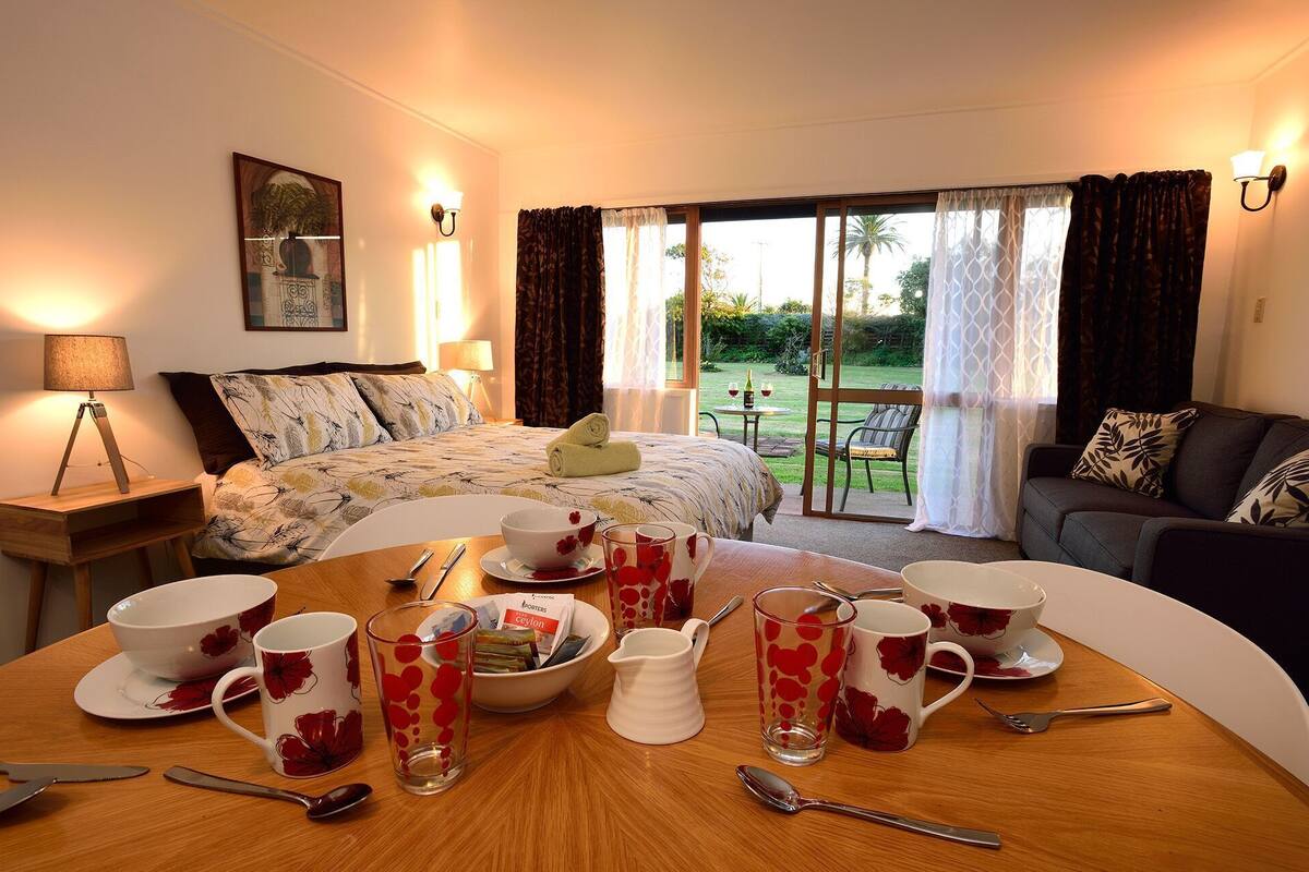 A hotel room with a bed, a dining table set with tableware, a sofa, and a view of the outdoors.