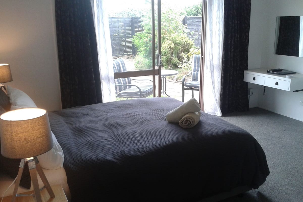 A hotel room with a bed, a desk, a lamp, and a view of the outdoors.