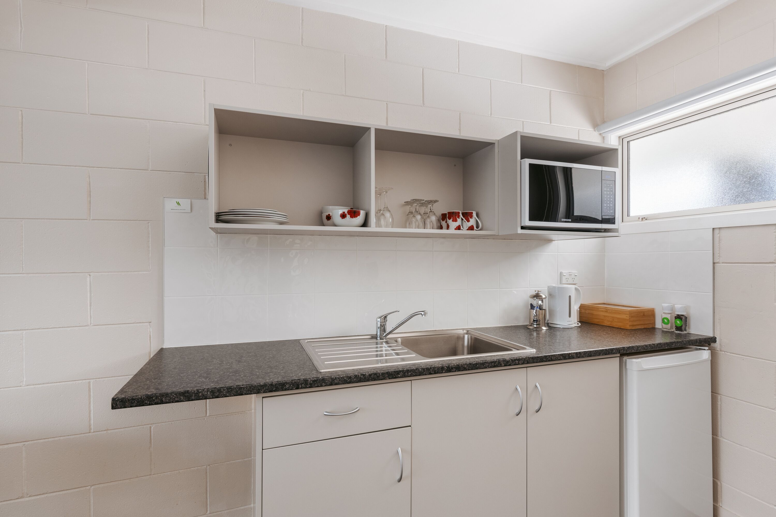 Eine Küche mit Granit Arbeitsplatte, Spüle aus Edelstahl, weißen Schränken und einer Mikrowelle über der Arbeitsfläche.