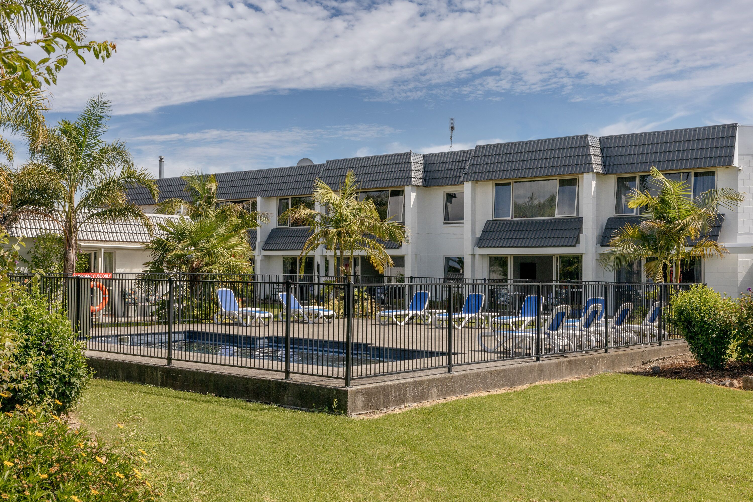 Un hotel moderno con zona de piscina, palmeras y un cielo azul despejado.