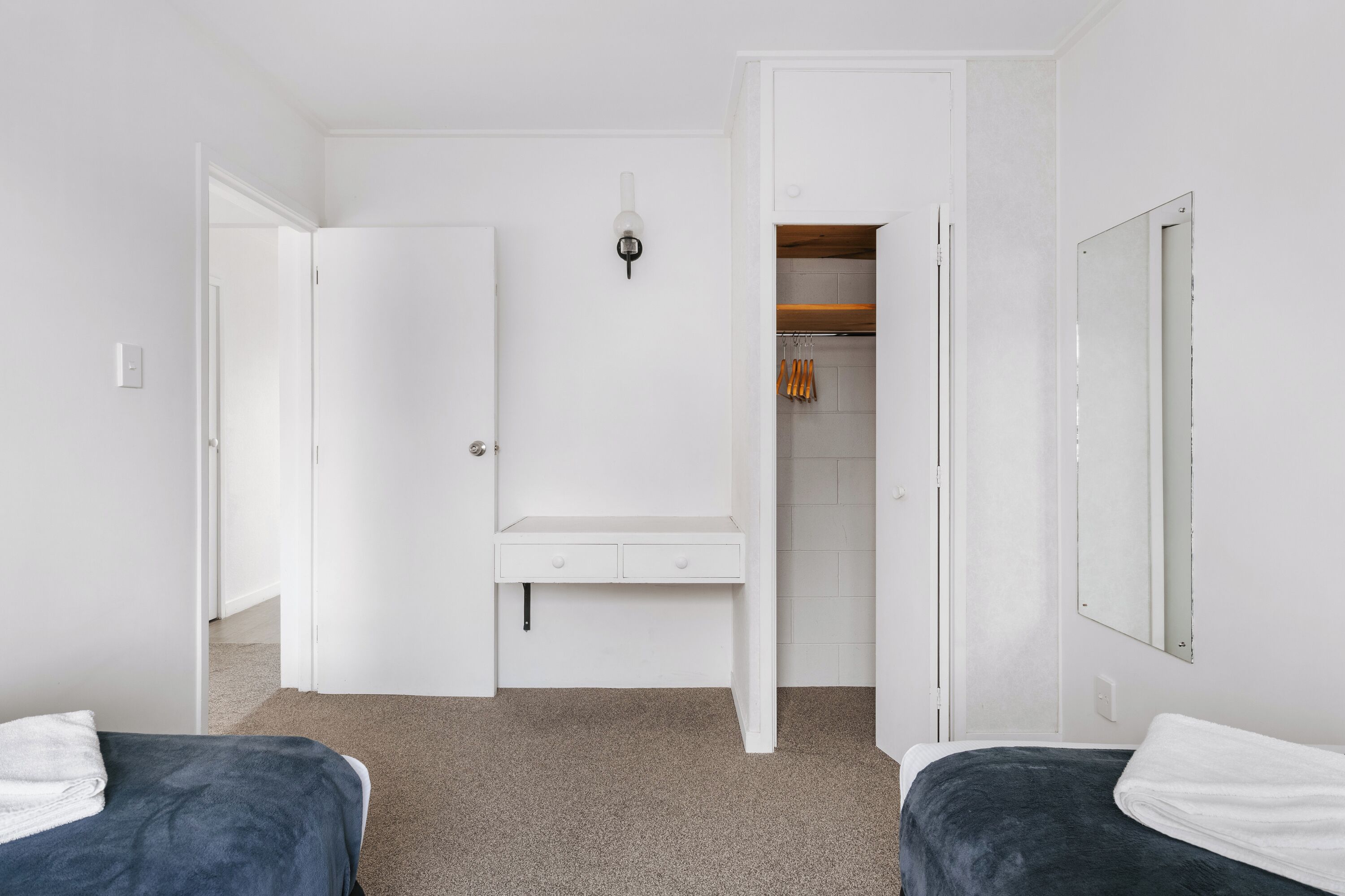 A bedroom with two beds, a white wardrobe, a mirror, and a closet with hanging clothes.