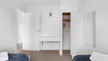 A bedroom with two beds, a white wardrobe, a mirror, and a closet with hanging clothes.