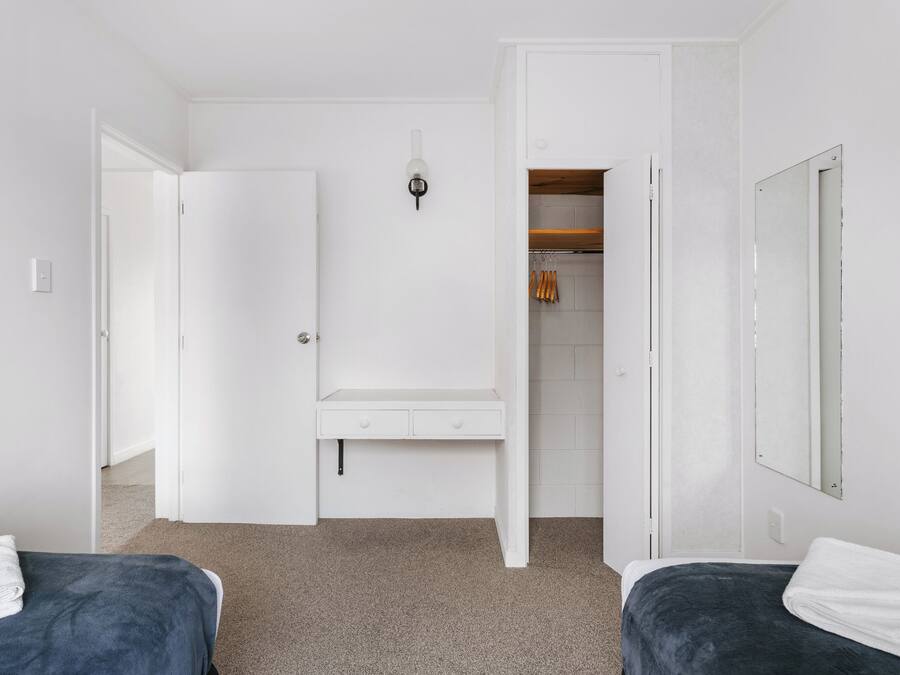 A bedroom with two beds, a white wardrobe, a mirror, and a closet with hanging clothes.