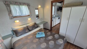 A bedroom with a bed, bedside tables, a mirror, a wardrobe, and a view into a kitchen area. - Bonnie Doon Caravan Park (Bonnie Doon)