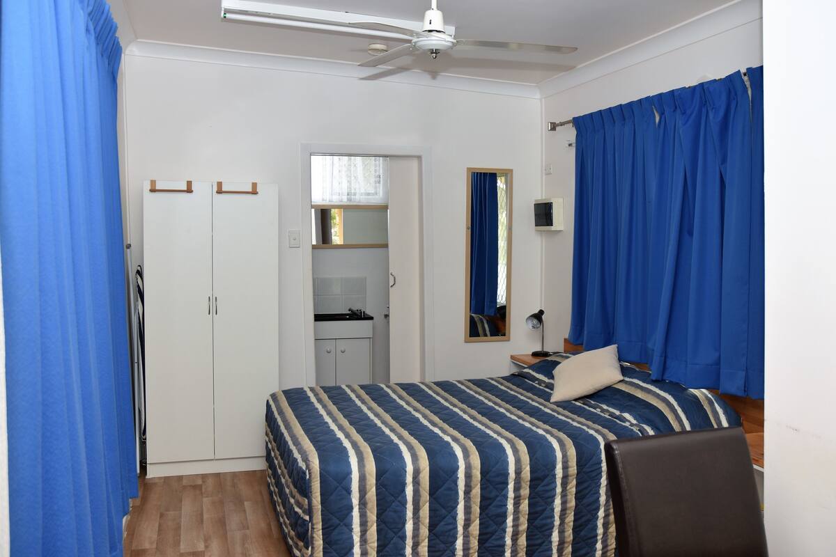 A bedroom with a bed, a wardrobe, a ceiling fan, and a bathroom visible through an open door.