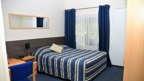 A hotel room with a bed, a desk with a chair, a mirror, and a window with curtains. - Chinchilla Motel (Chinchilla)