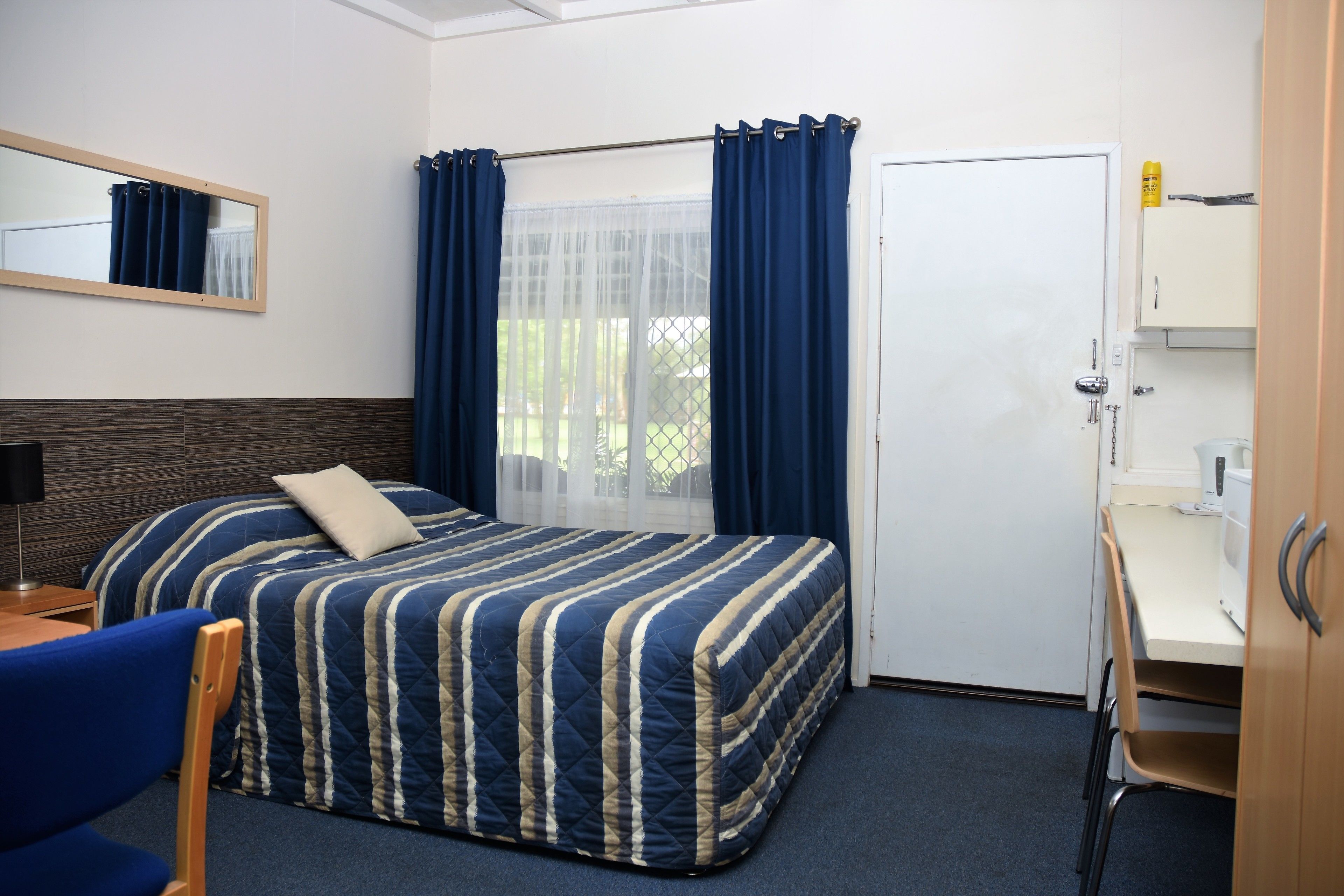 A hotel room with a bed, a desk, a chair, a mirror, and a wardrobe.