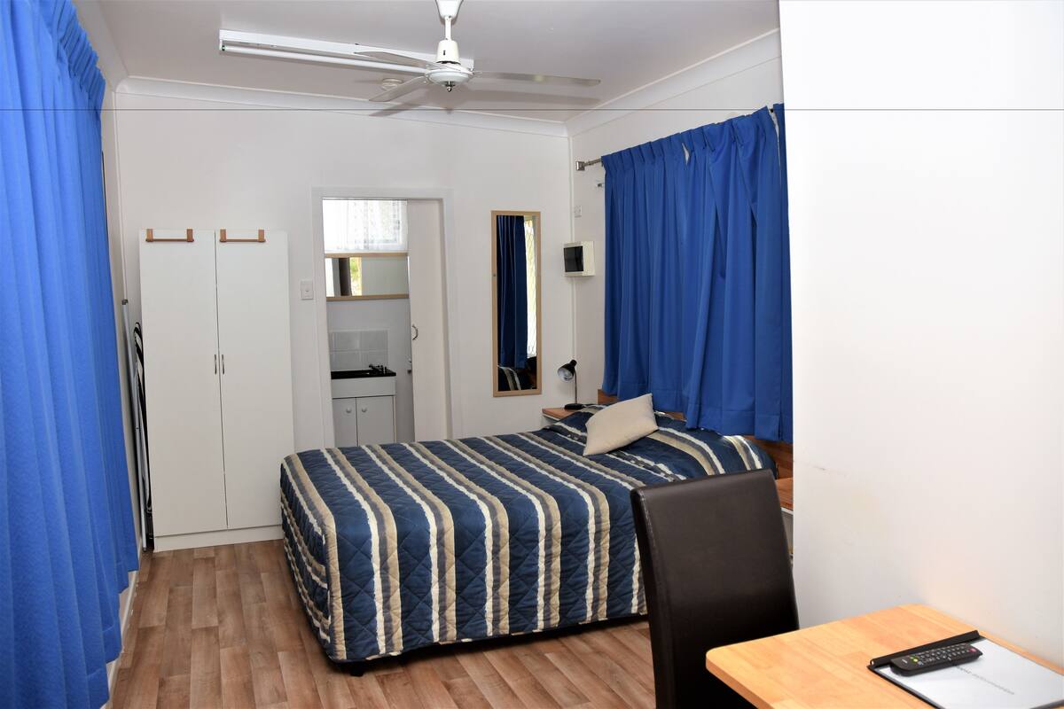 A bedroom with a bed, a desk, a chair, a ceiling fan, and a wardrobe.