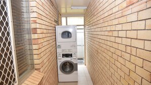 A narrow laundry room with a stacked washer and dryer, brick walls, and a tiled floor. - Chinchilla Motel (Chinchilla)