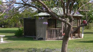 A gazebo with a wooden deck, surrounded by a grassy area with scattered flowers. - Chinchilla Motel (Chinchilla)