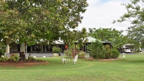 A grassy outdoor area with a table and chairs, surrounded by trees and a building in the background. - Chinchilla Motel (Chinchilla)