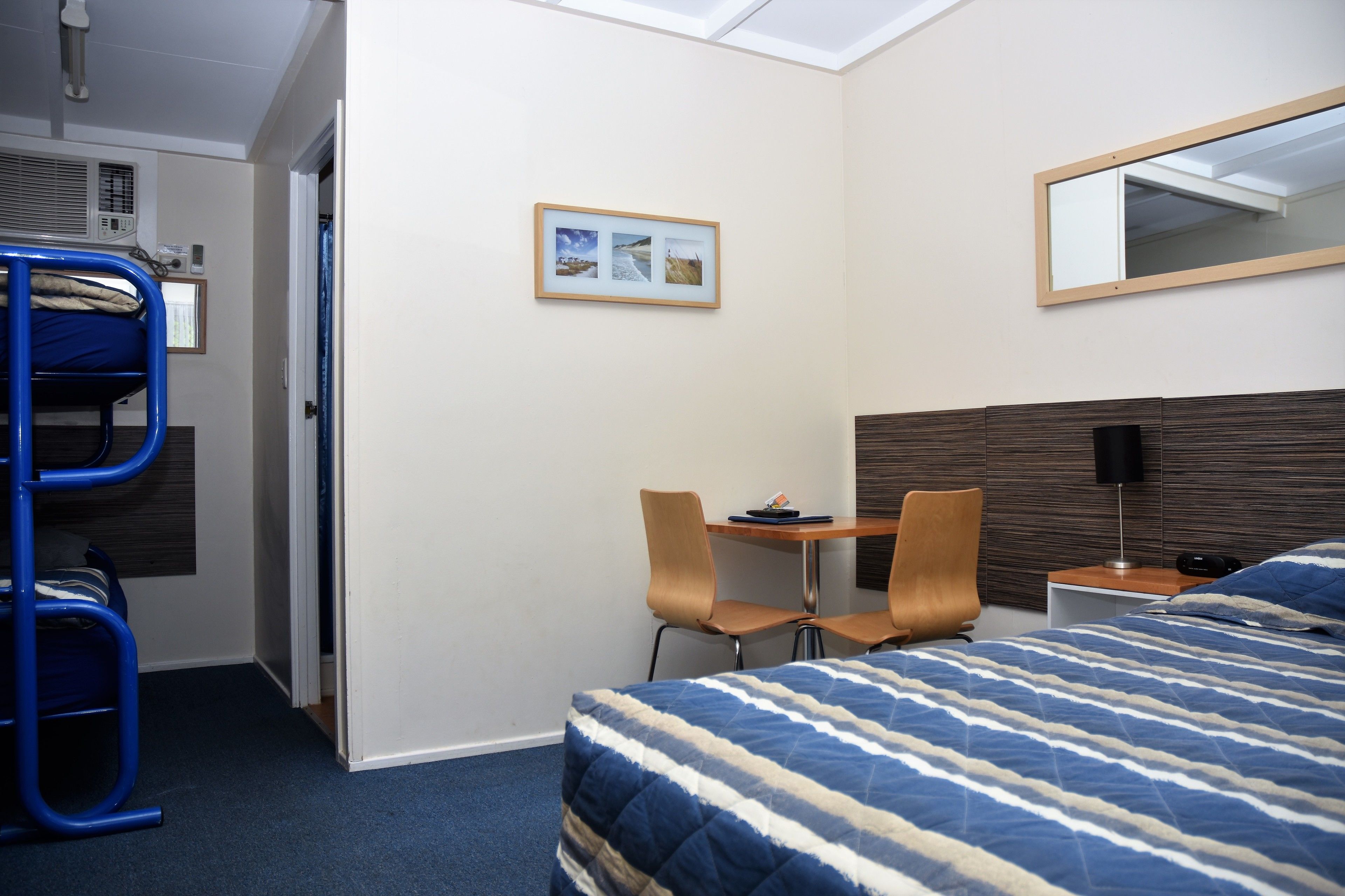 Ein Hotelzimmer mit Etagenbett, Schreibtisch mit zwei Stühlen, Nachttisch und einem großen Bett mit gestreifter Bettdecke.