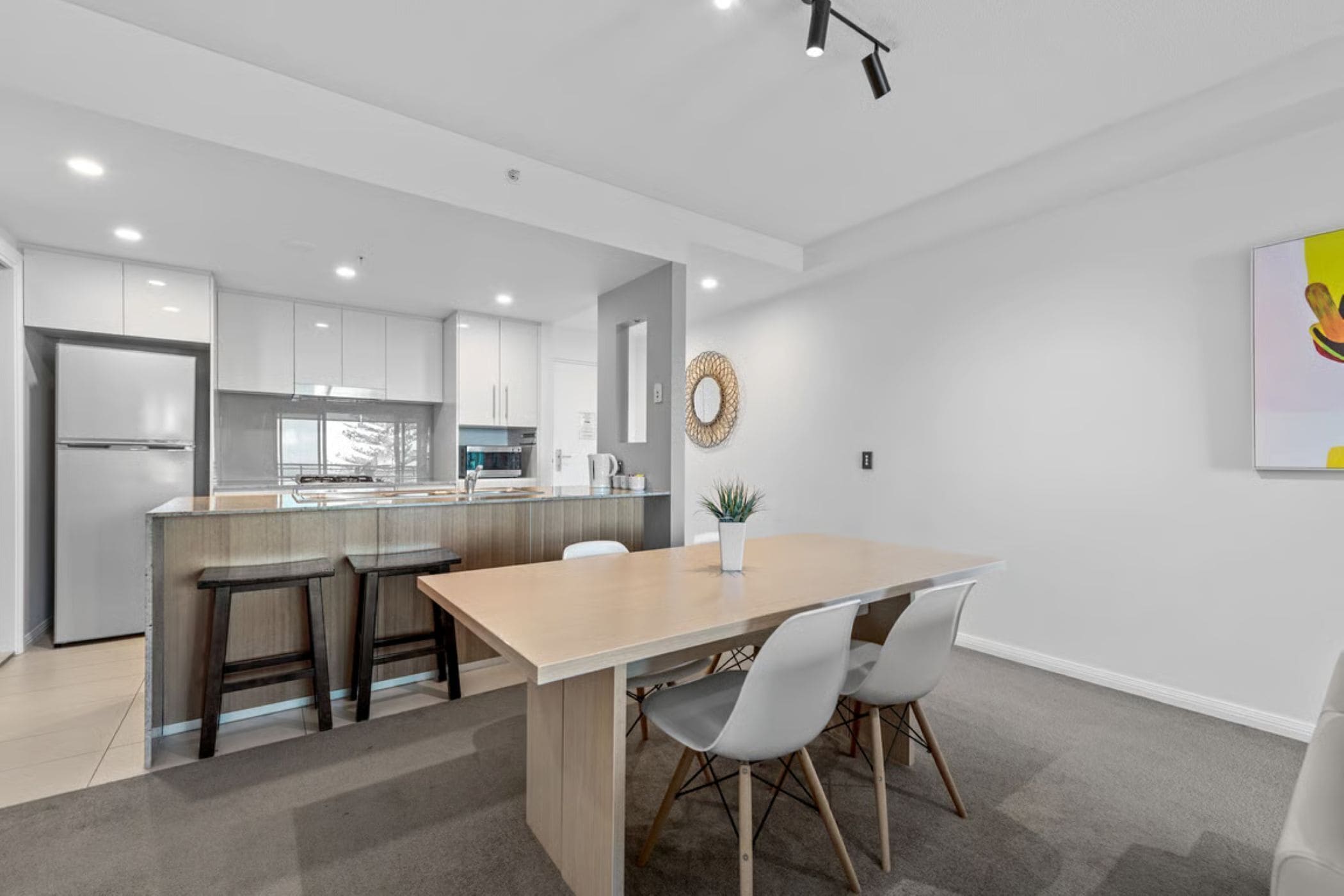 A modern kitchen with a central island, bar stools, and a dining table with chairs.