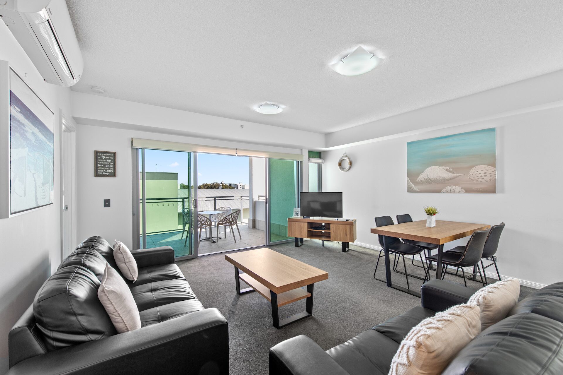 A modern living room with a sofa, a coffee table, a TV, and a dining area with chairs and a table.