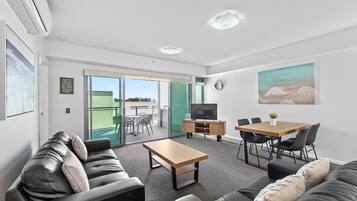 A modern living room with a sofa, a coffee table, a TV, and a dining area with chairs and a table.